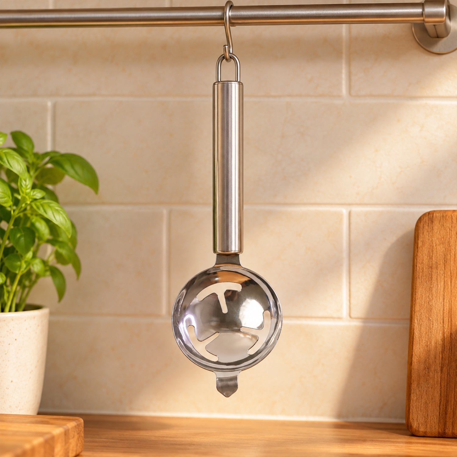 A stainless steel egg separator hangs from a metal rail against a tiled kitchen wall with a plant beside it.