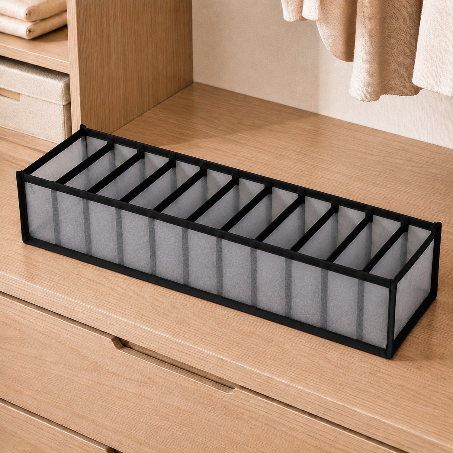 An empty gray 11-section fabric organizer with black trim sits on a light wooden dresser in a closet.