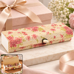 A rectangular bamboo box with a roll-top lid and pink floral pattern sits on a marble surface next to a pink gift box.