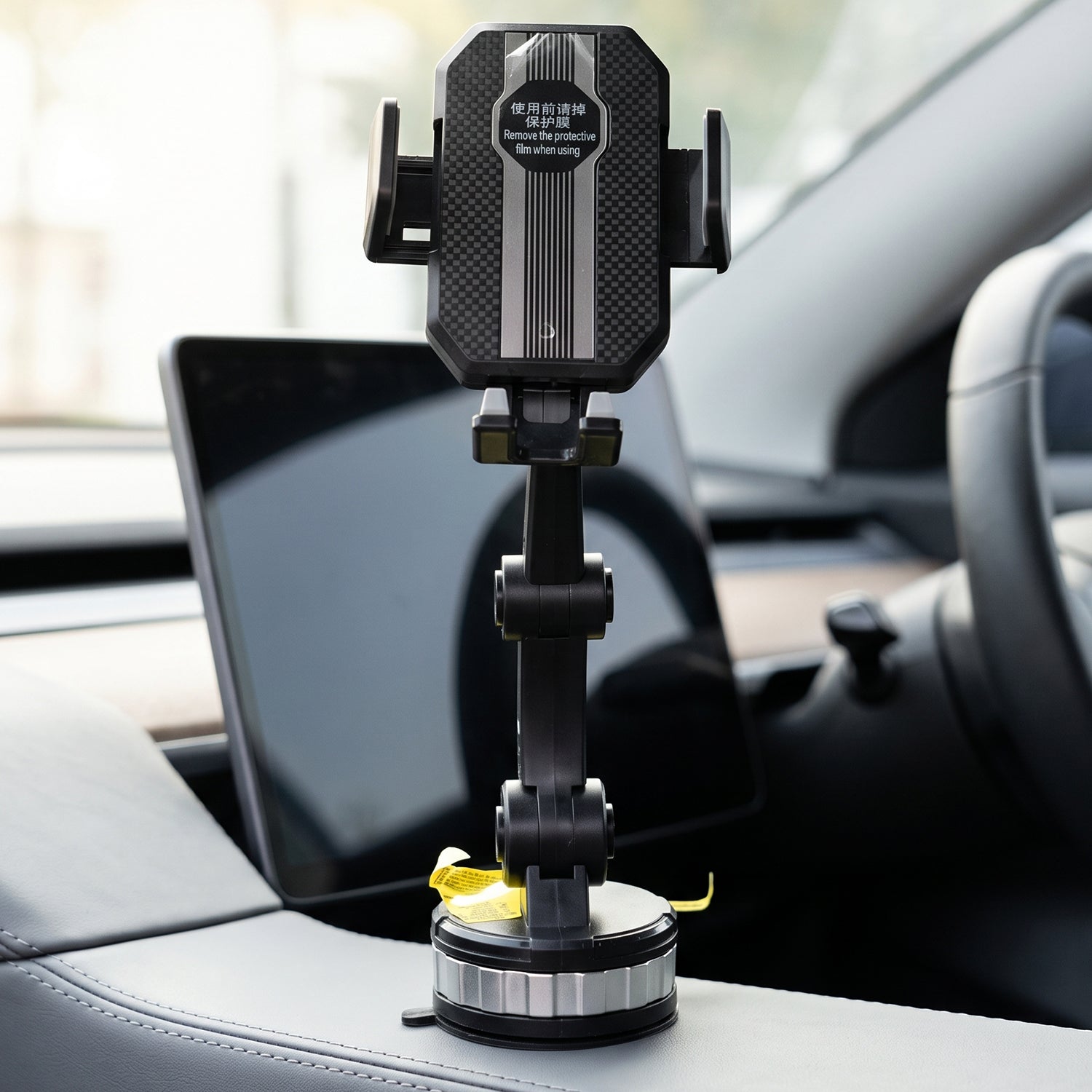 A black car mount phone holder with a textured back is positioned on a car's center console, with a tablet in the background.