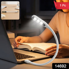 A person reading a book at night with a white flexible USB LED light plugged into a laptop, providing illumination.