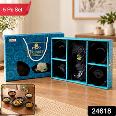 A blue patterned gift box containing a black leaf-shaped platter and four black bowls is on a wooden table.
