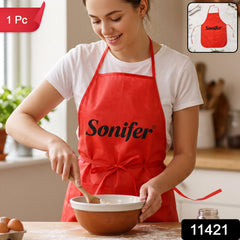 A smiling woman in a white t-shirt and a red Sonifer apron stirs batter in a bowl on a wooden counter, with