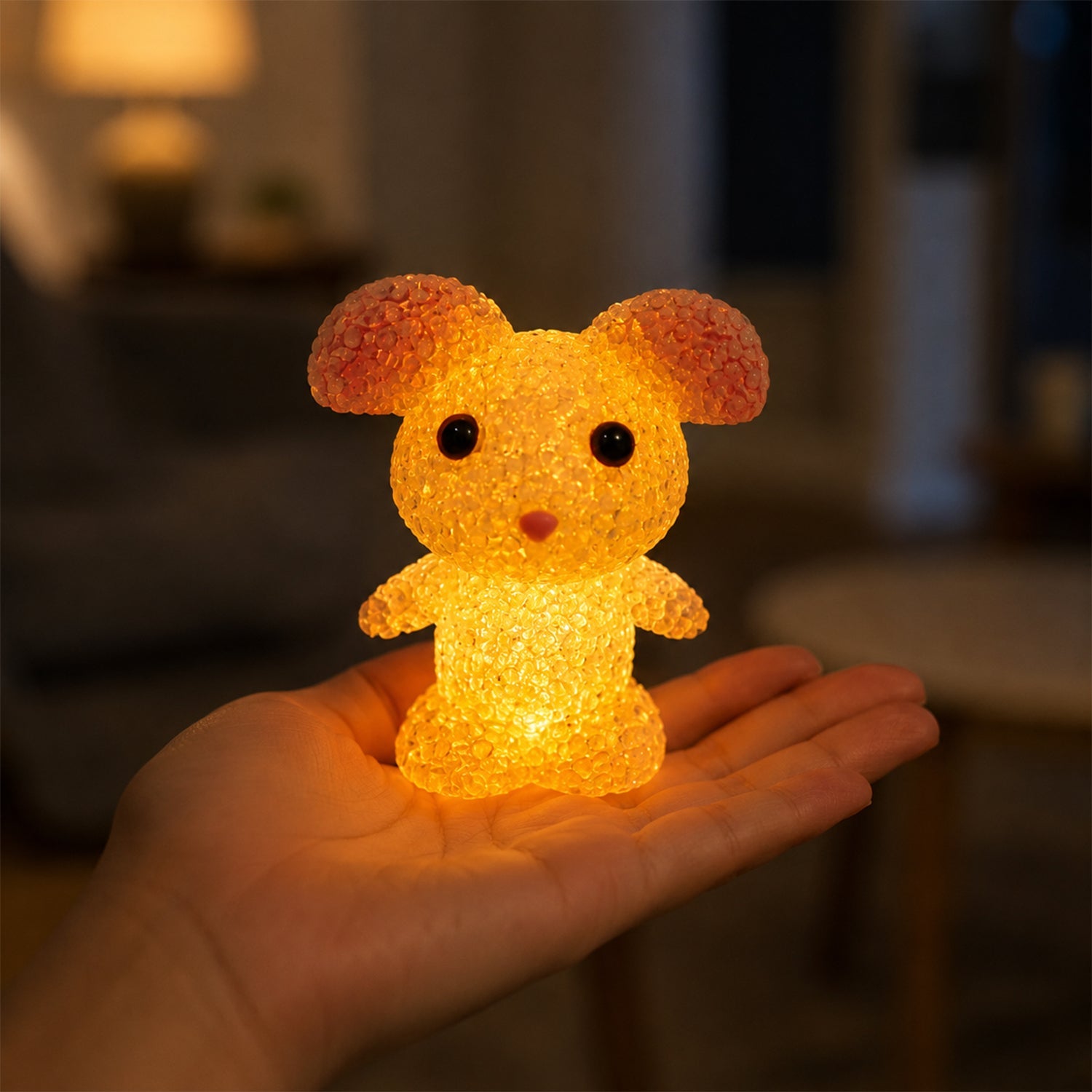 A yellow mouse-shaped crystal texture LED lamp glowing in the palm of a hand in a dimly lit room.