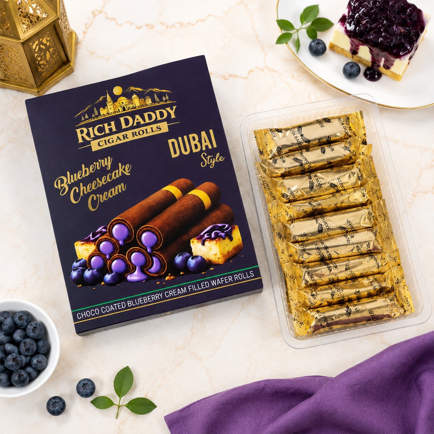 An open package of individually wrapped gold wafer rolls sits beside a Rich Daddy box, a bowl of blueberries, and a slice of