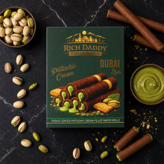 Green box of Rich Daddy Cigar Rolls, surrounded by pistachios and a bowl of green cream on a dark marble surface.